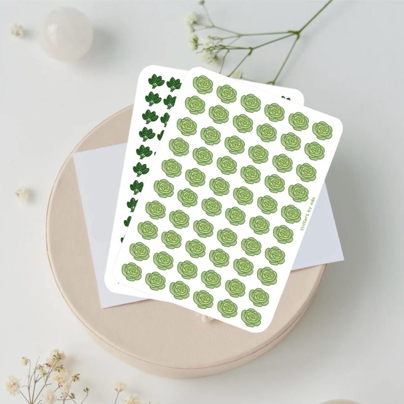 May include: Two rectangular sticker sheets featuring repeating patterns of small green vegetables. One sheet displays light green cabbage illustrations, while the other shows dark green broccoli florets. The text "stickers by ada" is printed on the side.