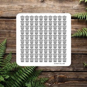 May include: A square white sticker sheet featuring a repeating pattern of small black trash can illustrations. The sticker sheet has rounded corners and the text "stickers by ada" in the bottom right corner.