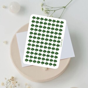 May include: A rectangular sticker sheet featuring a repeating pattern of small, dark green broccoli florets arranged in neat rows and columns. The text stickers by ada is printed in small, dark green letters along the right side of the sheet.