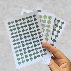 May include: Three white sticker sheets featuring repeating vegetable patterns in shades of green. The sheets display small illustrations of broccoli, lettuce, and broccoli florets. Each sheet includes the text stickers by ada printed on the side.