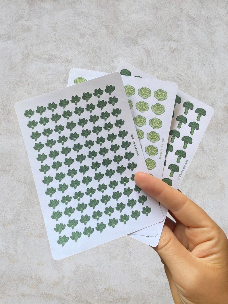 May include: Three white sticker sheets featuring repeating vegetable patterns in shades of green. The sheets display small illustrations of broccoli, lettuce, and broccoli florets. Each sheet includes the text stickers by ada printed on the side.