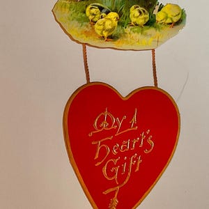 May include: Vintage Easter-themed hanging decoration with three sections. The top section has a floral design and the words "Love's Gift". The middle section features a wooden bucket, a puppy, and chicks. The bottom section is a red heart with the words "By A Heart's Gift".
