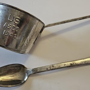 Peut inclure: Une tasse à mesurer et une cuillère en métal vintage. La tasse porte l'inscription "US ASCO 1942" et possède une poignée. La cuillère a un bol arrondi et un trou dans le manche. Les deux articles montrent des signes d'usure.