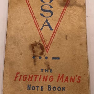 May include: A vintage rectangular notebook with a tan cover featuring a large red V, the blue text USA, and Morse code dots and dashes. The cover reads THE FIGHTING MAN'S NOTE BOOK, PEARL 12-7-41 HARBOR, and COPYRIGHT 1942 BY C. L. DARBY, with visible wear.