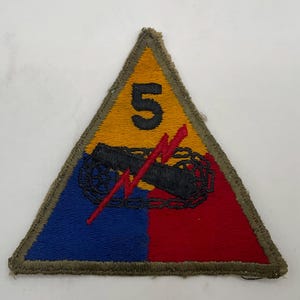 May include: A triangular embroidered patch featuring a yellow top section with a black number 5, a blue lower left section, and a red lower right section. A black tank tread graphic is centered with a red lightning bolt overlaying the design.