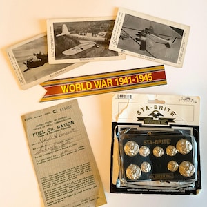 May include: A collection of vintage World War II memorabilia, including black and white photographs of airplanes, a ribbon with "WORLD WAR 1941-1945" printed on it, a fuel oil ration coupon, and a package of Sta-Brite buttons.