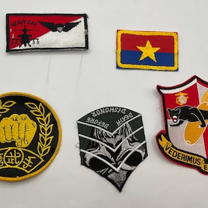 May include: Five embroidered patches including a rectangular patch with a helicopter and text HEAVY CAV, a red and blue rectangular patch with a yellow star, a circular black patch with a yellow fist, a chevron patch with text DEATH BEFORE DISHONOR, and a shield-shaped patch with a black panther and text VEDERIMUS ET DESTRUCTIMUS.