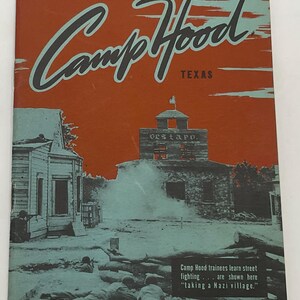 May include: A vintage booklet titled Camp Hood Texas with a bright orange sky and a monochrome scene of soldiers in training. The cover features a building labeled Gestapo and text stating Camp Hood trainees learn street fighting taking a Nazi village.