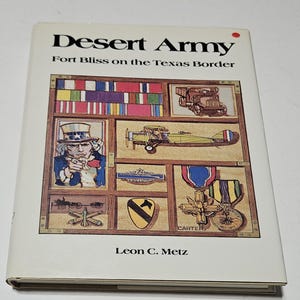 Può includere: Un libro con copertina rigida intitolato "Desert Army" con il sottotitolo "Fort Bliss on the Texas Border". La copertina presenta illustrazioni di medaglie militari, un aereo e Zio Sam.