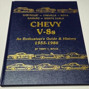 Puede incluir: Un libro azul marino con letras doradas e ilustraciones de coches. El título es "CHEVY V-8s", con el subtítulo "An Enthusiast's Guide & History 1955-1986" de Terry V. Boyce. La portada presenta modelos Chevrolet.