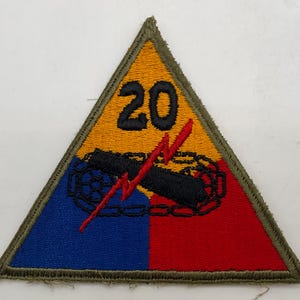 May include: A triangular embroidered patch featuring a yellow top section with the black number 20, a blue bottom left section, and a red bottom right section. A black tank tread graphic is centered with a red lightning bolt overlaying it.