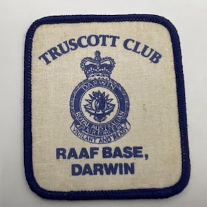 May include: A rectangular fabric patch with rounded corners, featuring a dark blue embroidered border on an off-white background. It displays the text TRUSCOTT CLUB, the Royal Australian Air Force emblem, and RAAF BASE, DARWIN in blue.