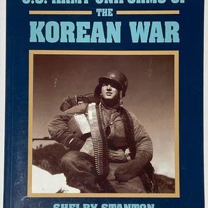 Könnte beinhalten: Ein Buch mit dem Titel "U.S. Army Uniforms of the Korean War" von Shelby Stanton. Das Cover zeigt eine Sepia-Fotografie eines Soldaten in Uniform, der einen Helm und einen Munitionsgürtel trägt. Das Buch hat einen dunkelblauen Einband mit weißem und beigem Text.