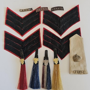 May include: A collection of vintage military insignia, including black chevrons with red trim, metal CANADA bars, and decorative tassels in various colors. A tan epaulette with a crown and CANADA text is also present.