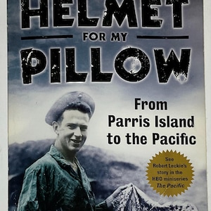 Könnte beinhalten: Buchcover für "Helmet for My Pillow" von Robert Leckie. Der Titel ist in großen, fetten Buchstaben geschrieben. Das Cover zeigt ein Schwarz-Weiß-Foto eines lächelnden Mannes in Militäruniform. Der Text enthält ein Zitat von Tom Hanks.