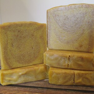 May include: Four bars of handmade soap, stacked in a pyramid shape. The soap is a light yellow color with a swirl pattern. The soap is sitting on a wooden surface.