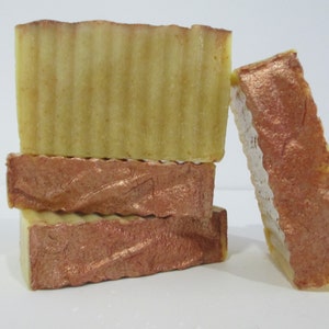 May include: Four bars of handmade soap, two with a light yellow color and a ridged texture, and two with a copper shimmer.