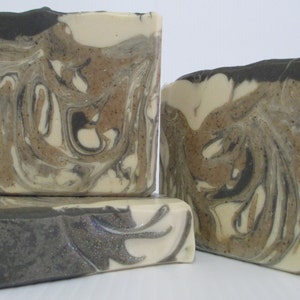May include: Three bars of handmade soap with a swirling pattern of black, white, and brown. The soap has a speckled appearance.