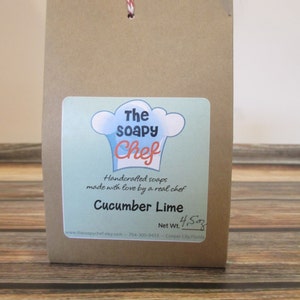 May include: A brown paper bag with a white string handle. The bag has a label that says "The Soapy Chef" and "Handcrafted soaps made with love by a real chef". The label also says "Cucumber Lime" and "Net Wt. 4.5 oz".