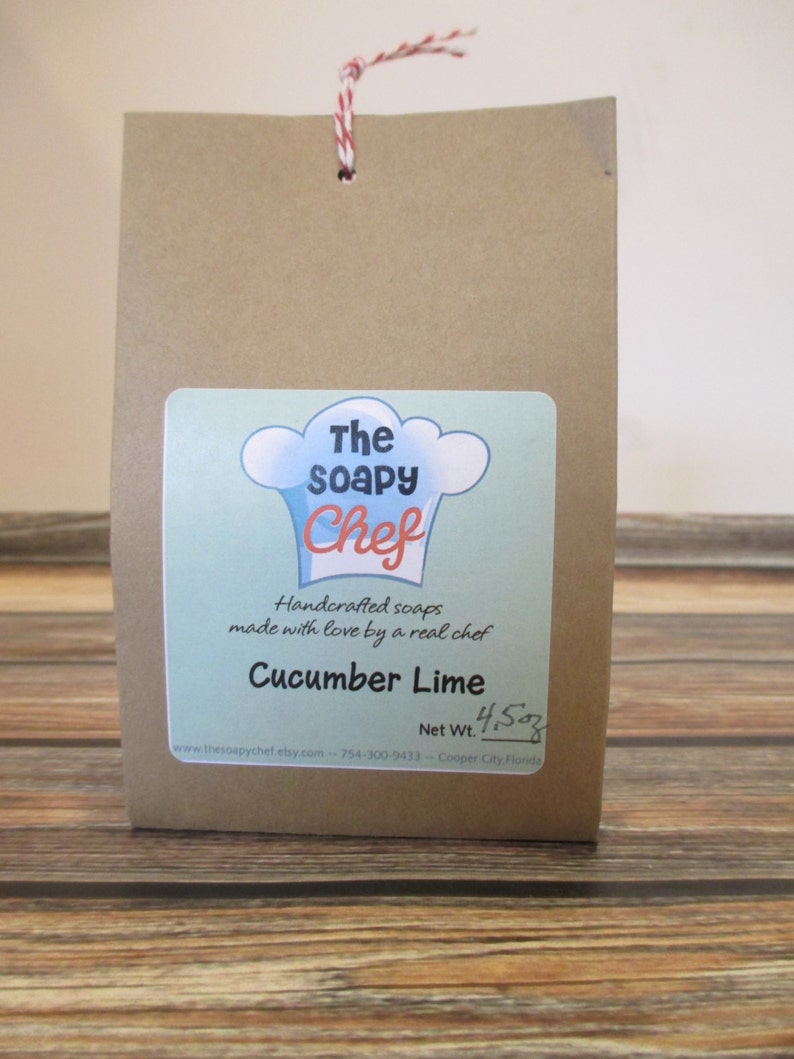 May include: A brown paper bag with a white string handle. The bag has a label that says "The Soapy Chef" and "Handcrafted soaps made with love by a real chef". The label also says "Cucumber Lime" and "Net Wt. 4.5 oz".