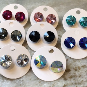 May include: Assortment of round crystal earrings in various colors, including pink, blue, black, and clear. The earrings are displayed on white circular cards with a hole for hanging.