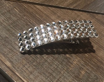 May include: A silver hair clip with a rectangular shape covered in clear rhinestones.