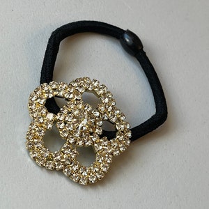 May include: A black elastic hair tie with a gold-toned, rhinestone-encrusted flower-shaped embellishment.