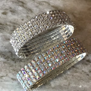 May include: Two silver stretch bracelets with rows of clear and iridescent rhinestones. The bracelets are stacked on top of each other.