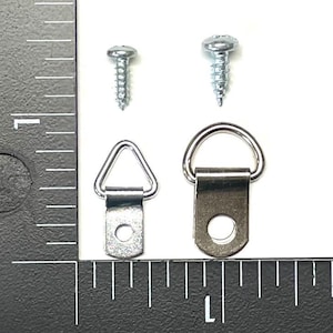 May include: Two silver-toned D-ring picture hangers and two silver screws. The D-rings are different sizes. The smaller D-ring is triangular shaped.