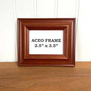 May include: A brown wooden ACEO frame, 2.5" x 3.5", with a rectangular opening. The frame has a detailed, ridged border and is displayed on a wooden surface against a white background.