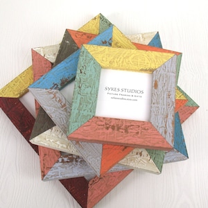 May include: A collection of colorful, geometric picture frames. The frames are made of wood and painted in various shades, including red, yellow, blue, and orange. The frames have a distressed, rustic look and the text "SYKES STUDIOS" is visible.