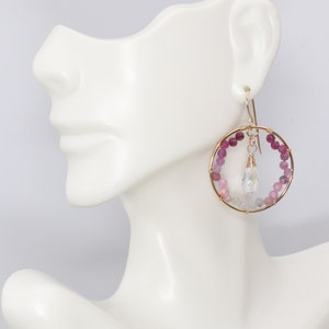May include: Gold hoop earrings with a teardrop crystal and pink and purple gemstone beads.