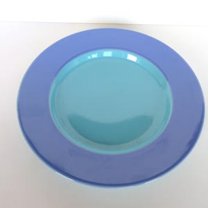 May include: A round, two-toned plate with a light blue center and a darker blue rim. The plate is made of ceramic or porcelain and is suitable for serving food. The plate is a simple, yet elegant design.