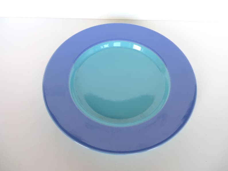 May include: A round, two-toned plate with a light blue center and a darker blue rim. The plate is made of ceramic or porcelain and is suitable for serving food. The plate is a simple, yet elegant design.