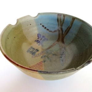 May include: A large, ceramic bowl with a green, blue, and brown glaze. The bowl has a tree and flower design painted on the inside.