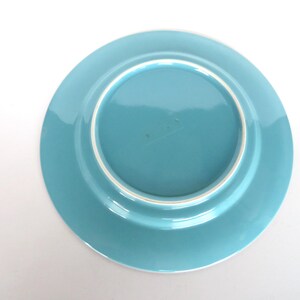 May include: A turquoise ceramic plate with a white rim. The plate is round and has a slightly raised edge. The underside of the plate is visible, showing a smooth, glossy finish.