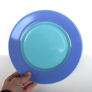 May include: A two-toned plate with a light blue center and a periwinkle rim. The plate is round and has a glossy finish. The plate is held by a hand.