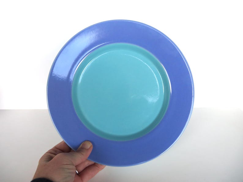 May include: A two-toned plate with a light blue center and a periwinkle rim. The plate is round and has a glossy finish. The plate is held by a hand.