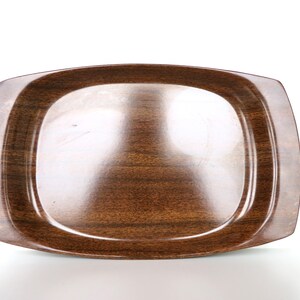 May include: A brown wooden tray with a slightly rounded rectangular shape. The tray has a smooth, glossy finish.