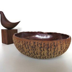 May include: A large, brown ceramic bowl with a textured surface. The bowl has a slightly iridescent glaze and is oval in shape.