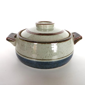 May include: A ceramic lidded pot with two handles. The pot is speckled with a light beige color, with a dark blue band around the base and a brown band around the lid. The handles and lid rim are brown.