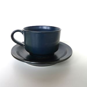 May include: A dark blue ceramic teacup and saucer set. The cup has a rounded shape and a handle. The saucer is a simple round shape.