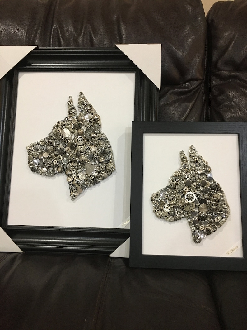 May include: Two framed black and white dog portraits made of buttons and other small metal objects. The larger portrait is on the left and the smaller portrait is on the right.
