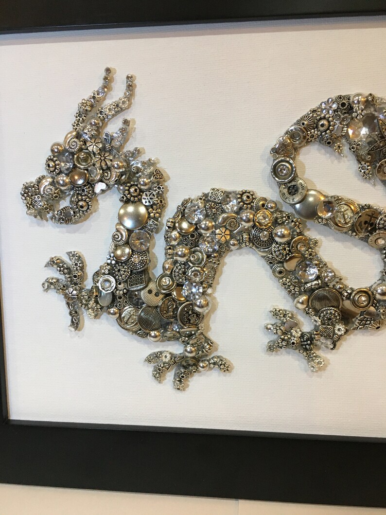May include: A silver and white dragon made of buttons and beads. The dragon is curled up in a defensive position with its head raised and its claws extended.