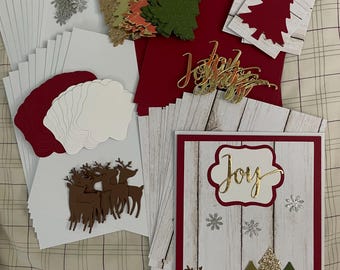 May include: A collection of Christmas-themed craft supplies, including red and white cardstock, decorative trees, reindeer, and the word "Joy" in gold script. The image showcases various elements for creating holiday cards and decorations.