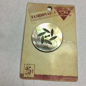 May include: A vintage button with a leaf design on a card that reads "Fashionable Le Chic Buttons" and "25c". The button is made of iridescent mother-of-pearl and has a dark brown hole in the center.