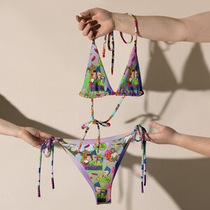May include: A colourful bikini with a triangle top and a high-cut bottom. The bikini is printed with a pattern of cartoon characters and the words "Posers!" and "Rockers!"
