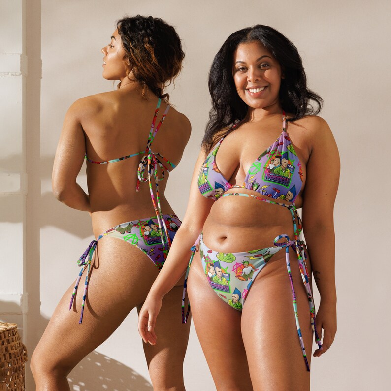 May include: Two women wearing colourful bikini tops and bottoms with a cartoon graphic print. The bikini tops are triangle shaped and the bottoms are tie-side.