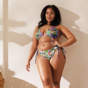 May include: A woman wearing a colourful patterned bikini top and bottom. The bikini has a purple, green and blue colour scheme with a cartoon graphic print.