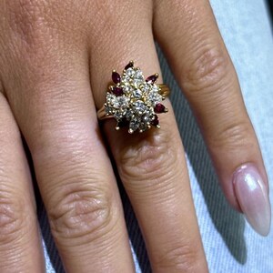 May include: A gold ring featuring a cluster of small white diamonds and red gemstones arranged in a flower-like design.